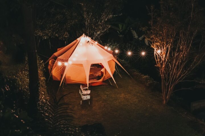 Glowing canvas glamping tent strung with lights at night in a garden, two chairs out front