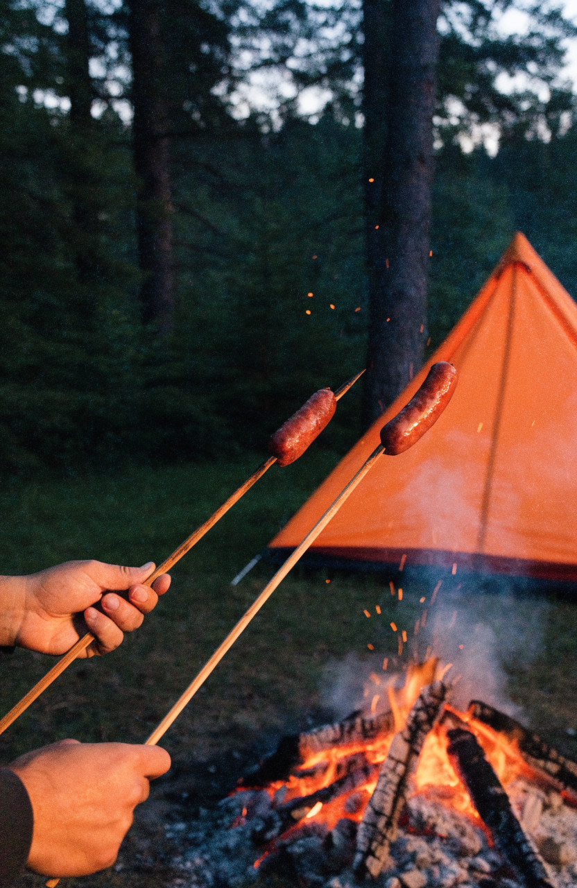 Hot dogs roasting on sticks over a campfire
