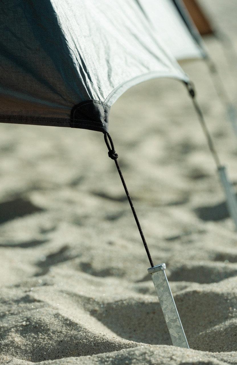 Tent guyline secured to angled sand stake in loose beach sand
