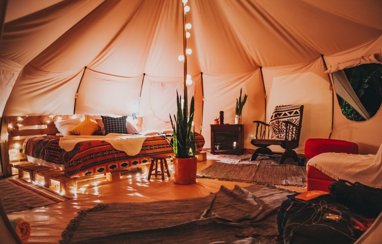 Bell tent interior with a pallet bed, string lights on the centre pole, rugs, plants and a rocking chair