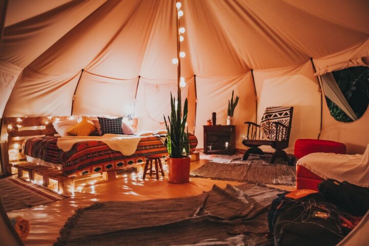 Bell tent interior with a pallet bed, string lights on the centre pole, rugs, plants and a rocking chair