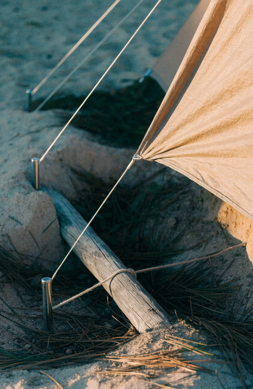 Tent guylines secured to angled stakes and buried anchor in sand