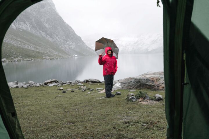 View from a tent doorway of a woman in a red rain jacket with an umbrella by a misty mountain lake