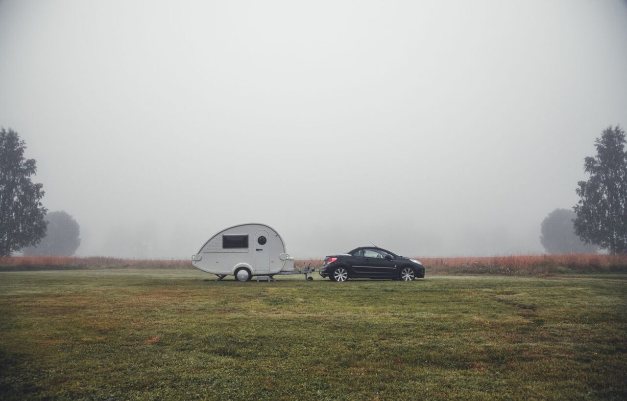 Small teardrop camper trailer hitched to a black car on a misty grass field