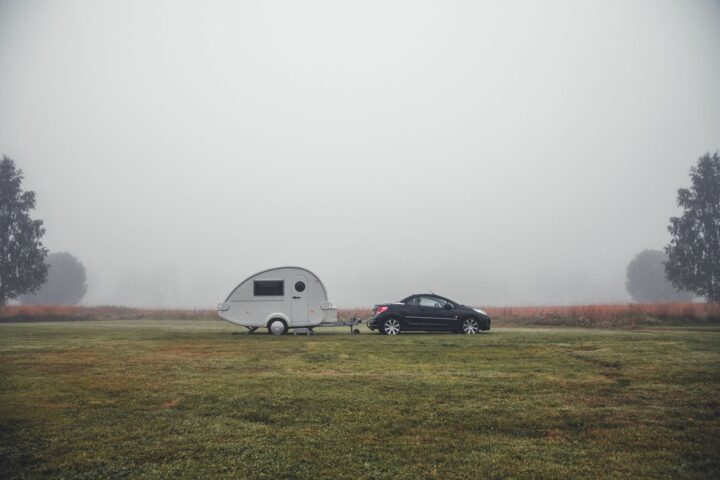 Small teardrop camper trailer hitched to a black car on a misty grass field