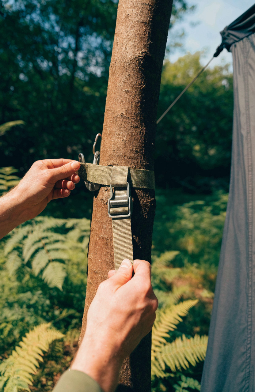 Hands securing wide tree strap and ratchet for suspended tent setup