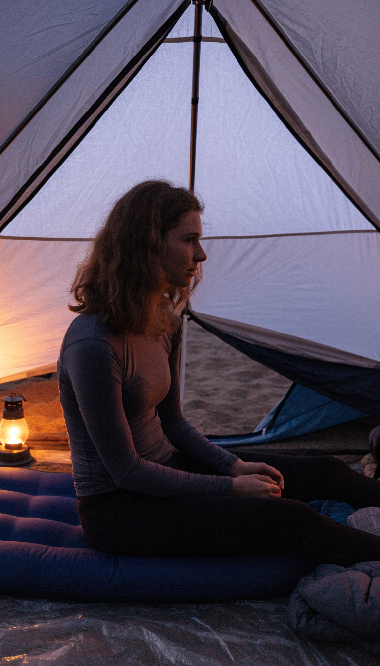 Woman in dark long-sleeve top and leggings sitting inside a beach camping tent