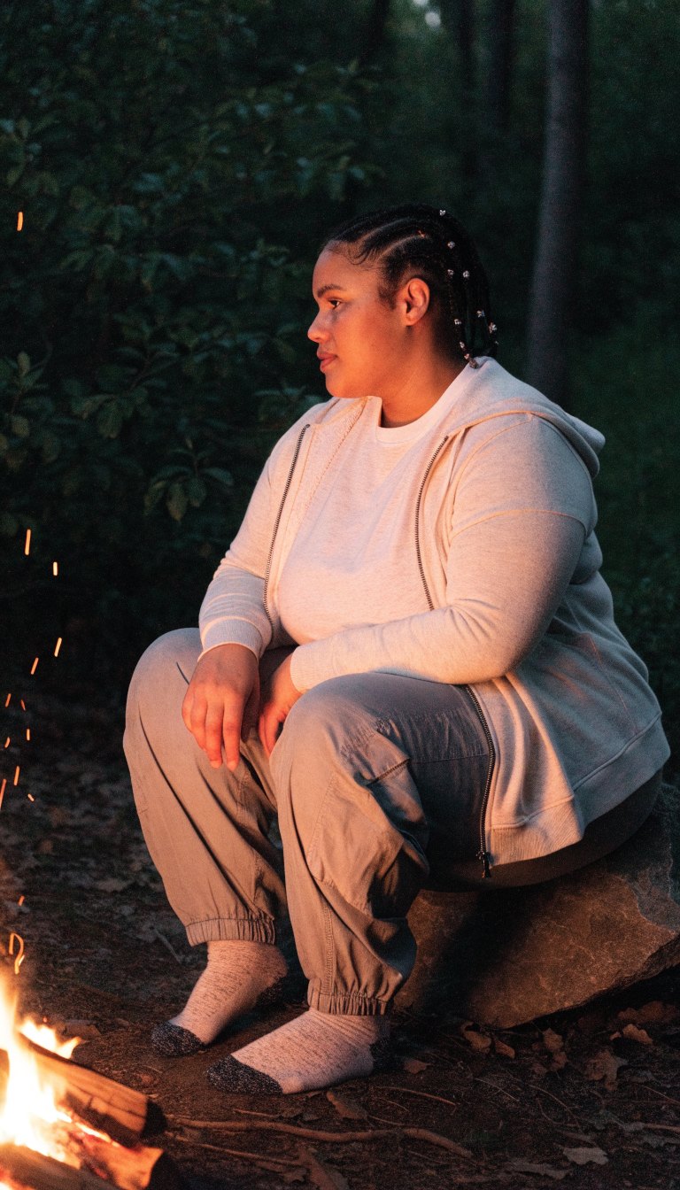 Plus-size woman in tee and joggers by a campfire at night