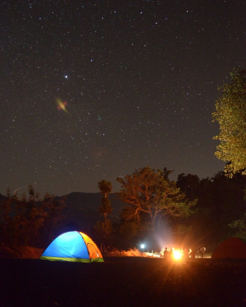 Lit dome tent and campfire under a starry sky